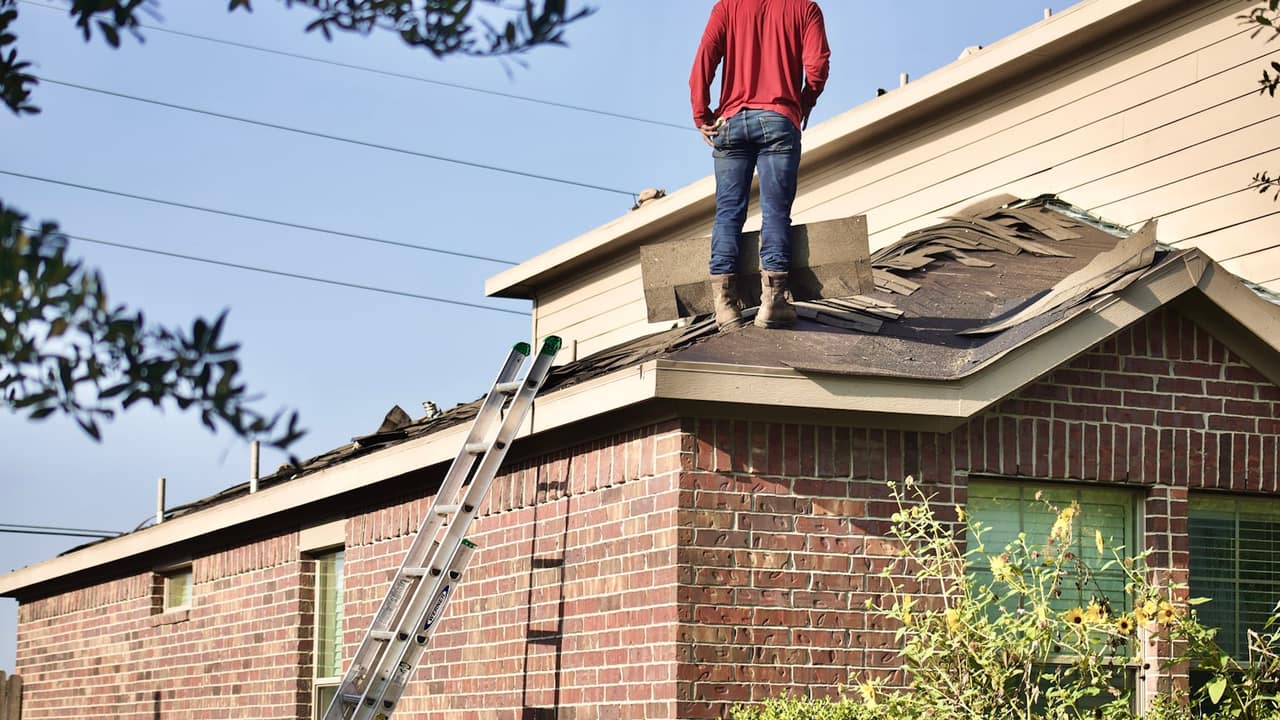 A roofer standing on the roof of a brick house during a re-roof