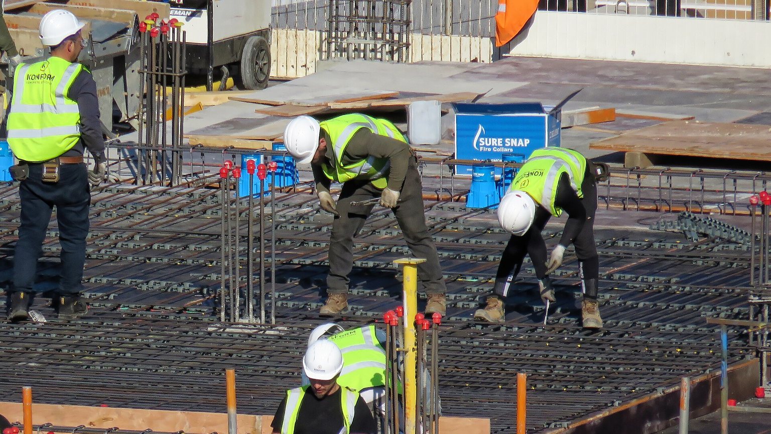 Workers tying rebar on a concrete deck at a construction site