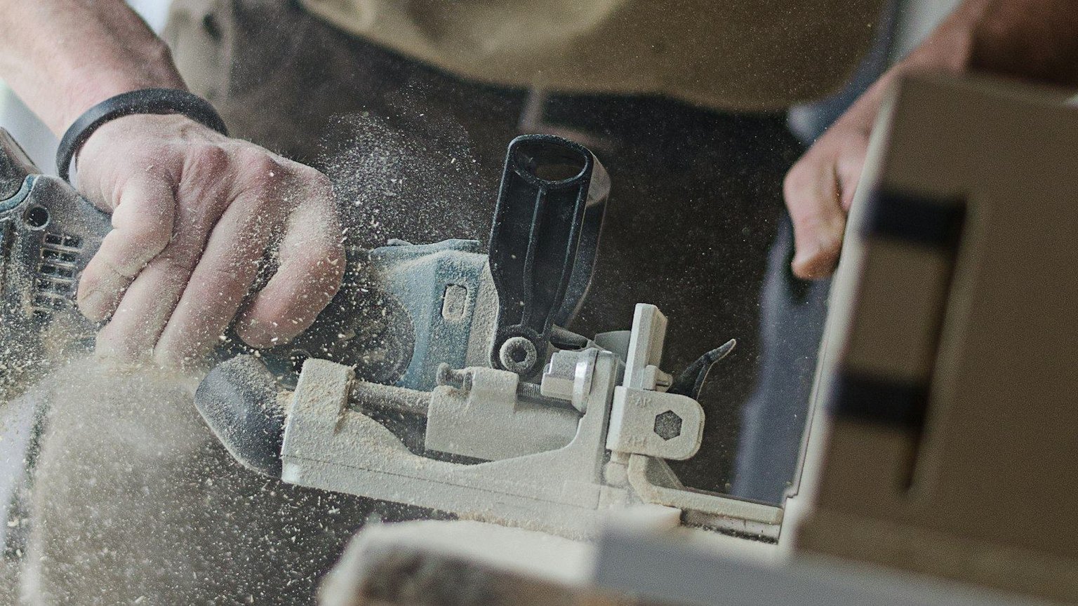 Close-up of a woodworker's hands using a biscuit joiner on cabinetry stock